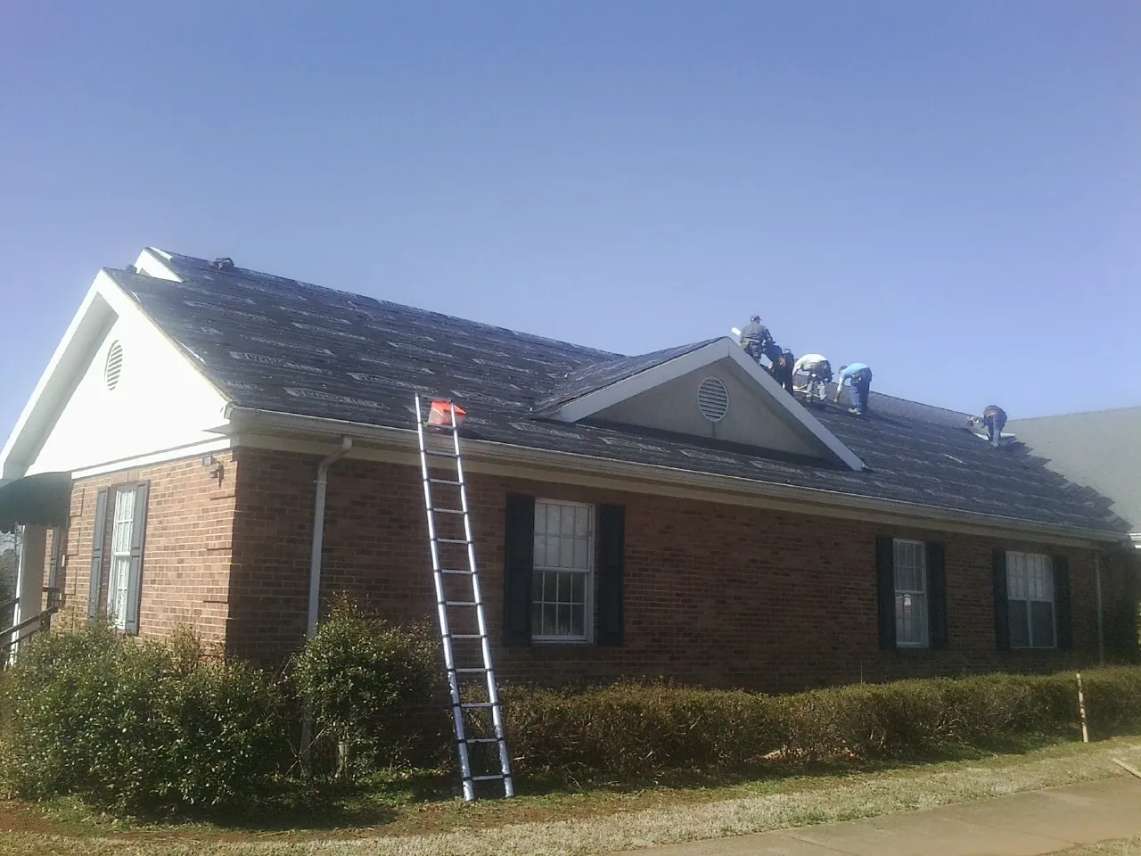 Crew tearing shingles off a brick ranch roof with a ladder set — Emergency Roof Repair work by our crew in North Versailles