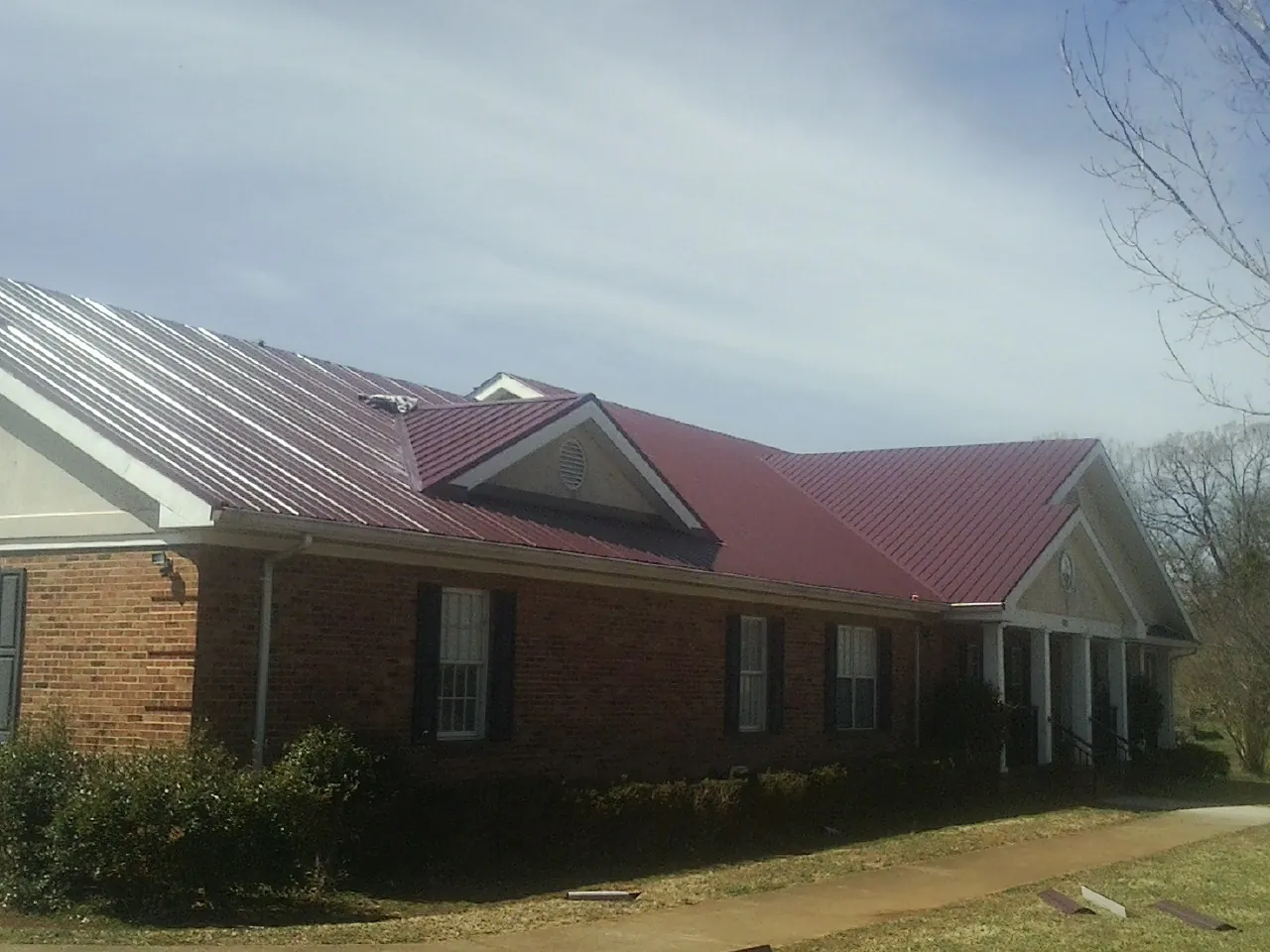 Red metal roof with gabled entries on a long brick building, from a Hail Damage Roof Repair job in North Versailles