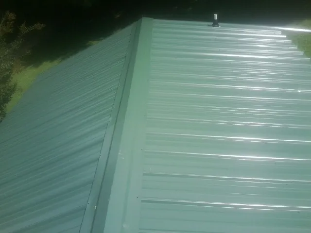 New green metal panels meeting at the ridge of a roof — Flat Roof Repair work by our crew in North Versailles
