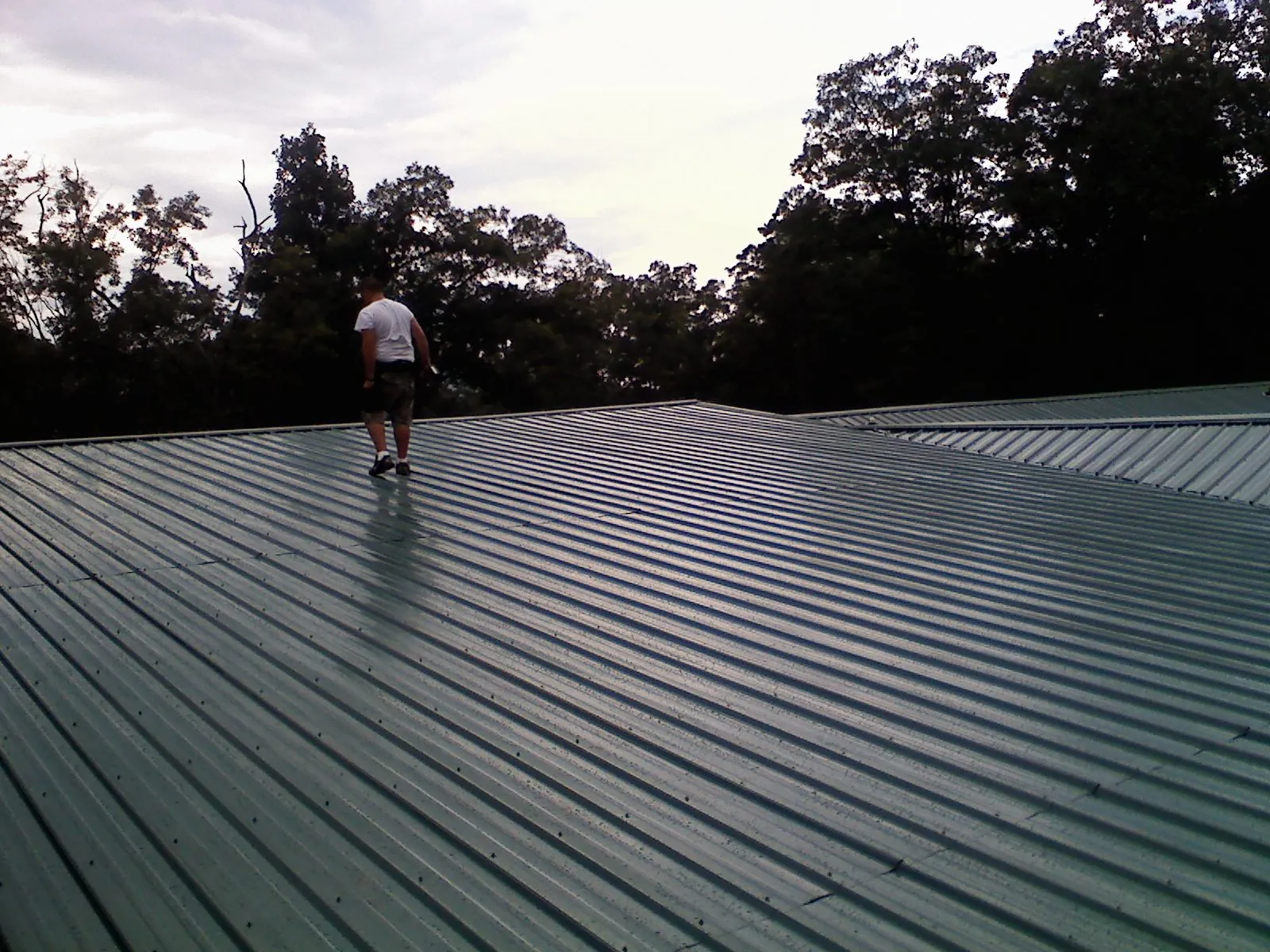 Roofer walking a wide expanse of new green metal roofing in North Versailles