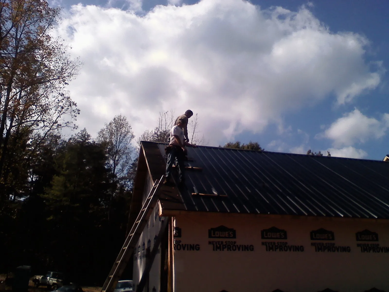 Roofer fastening dark metal panels high against a cloudy sky, from a Roof Inspection job in North Versailles
