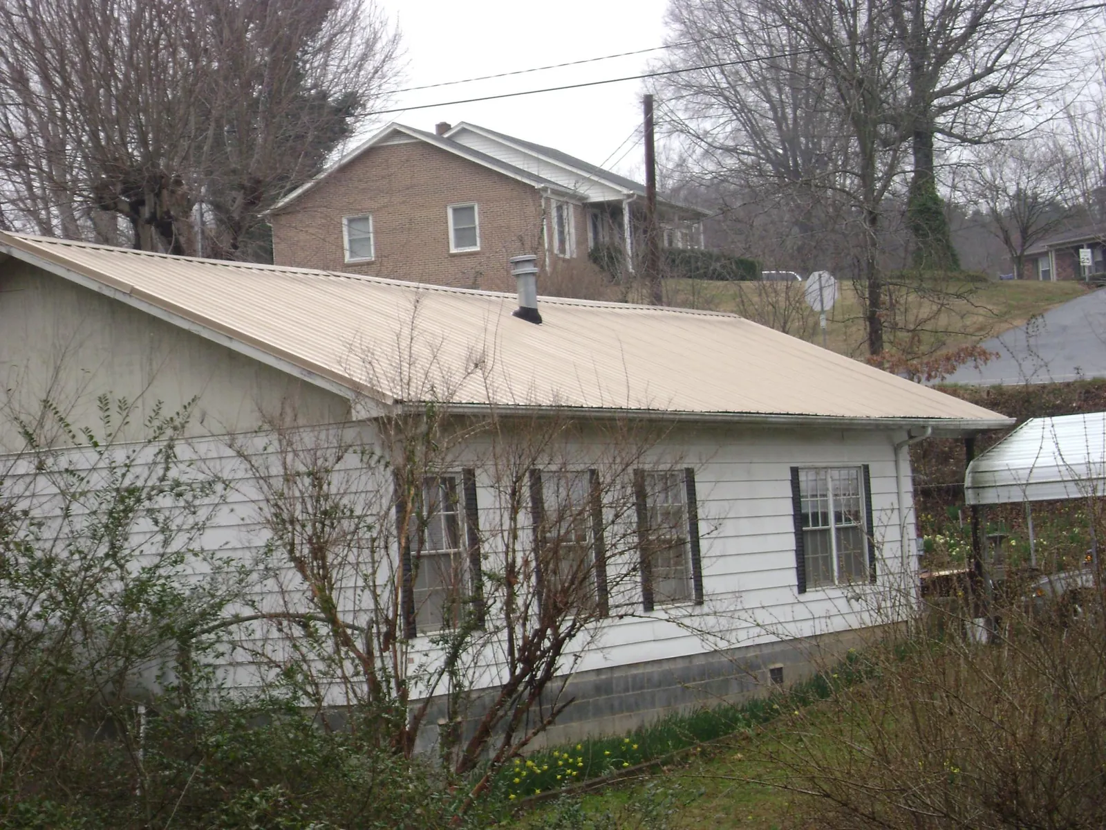 Tan metal roof on a white sided house set into a hillside — Commercial Roofing by Roofing Brothers in North Versailles